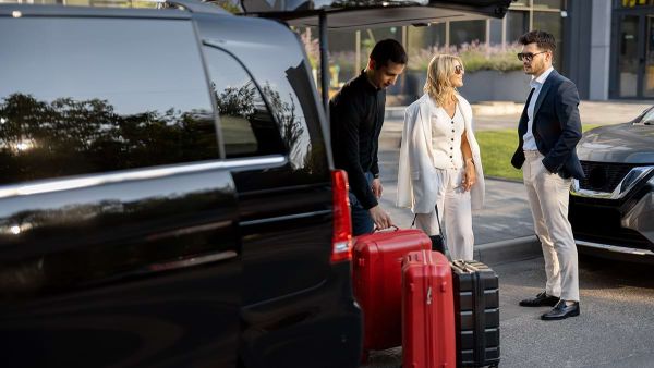 Parcheggio in Aeroporto. Coppia con bagagli e addetto al Car Valet in procinto di caricare le valigie su un van nero